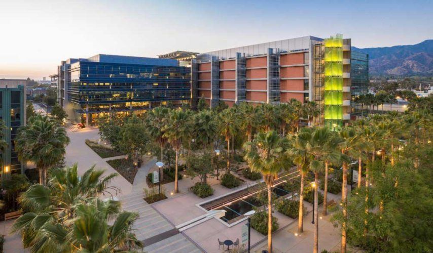 Concept drawing of the Grand Central Creative Campus, a modern 6-storey L-shaped building sitting behind landscaped palm trees